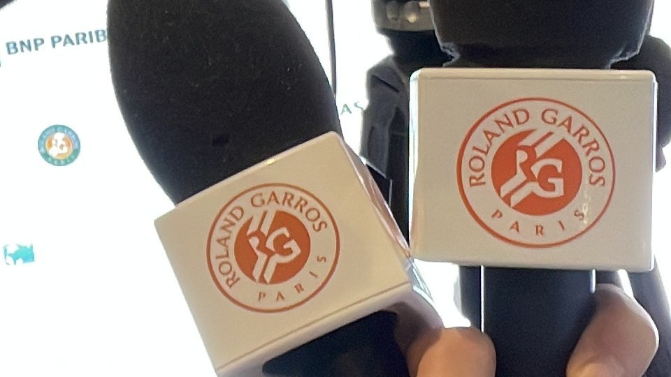 Deux micros aux couleurs de Roland-Garros tenus en main en salle de presse